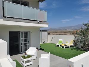 a patio with white chairs and a lawn at Divino en playa in Granadilla de Abona