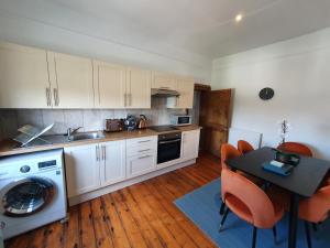 a kitchen with white cabinets and a table with orange chairs at Stylish City Centre Apartment on the Kings Mile in Canterbury