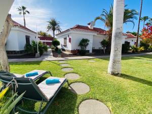 a lawn with two lounge chairs and a palm tree at Parque Golf 16 by SunHousesCanarias in Maspalomas