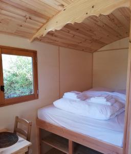 Cama en habitación pequeña con ventana en La Roulotte du Herdal en Profondeville