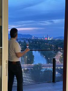 Un uomo che tiene un bicchiere di vino e guarda fuori da una finestra. di Royal Swan Skyline, Wien a Vienna