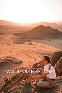 a woman sitting on a rock in the desert at Wadi Rum Fire Camp in Wadi Rum