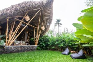 a building with a straw roof and some green grass at Balikayanas Bamboo House - Miggiell House in Karangasem