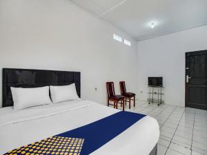 a bedroom with a bed and two chairs and a tv at SPOT ON 91117 Sriwijaya Residence Syariah in Bandung
