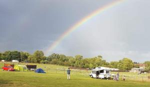 a rainbow over a field with a man and tents at Two Jays Farm in Norwich