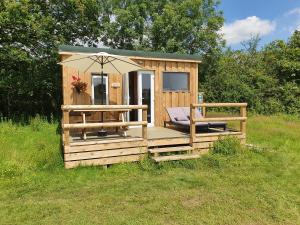 uma cabina de madeira com um guarda-chuva e uma cadeira em Dartmoor Reach Alpaca Farm Heated Cabins 5 mins drive to Dartmoor em Bovey Tracey