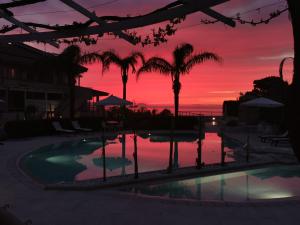 a sunset over a swimming pool with palm trees at L' Arcobaleno Resort in Capo Vaticano