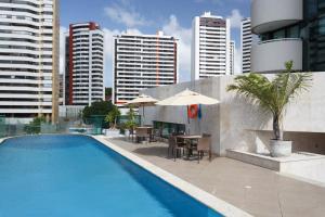a swimming pool with tables and umbrellas in a city at Mercure Salvador Pituba in Salvador