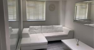 a living room with a white couch and a clock at Luxurious high spec 1 bedroom apartment in London in Eltham