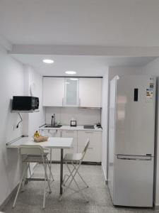 a white kitchen with a table and a refrigerator at Anatolia playa Jardin PUERTO DE LA CRUZ Estudio in Puerto de la Cruz