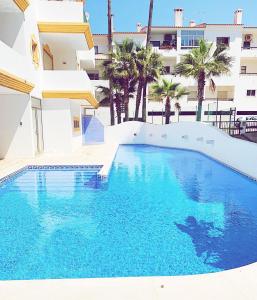 a swimming pool in front of a building with palm trees at Albufeira Central Apartment, 10 mins walk to beach in Albufeira