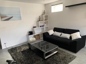 ein Wohnzimmer mit einem schwarzen Sofa und einem Tisch in der Unterkunft Appartement 5 personnes avec accès piscine in Thyle