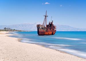 an old boat sitting on the shore of a beach at The Olive Yard in Gythio