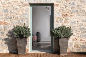 otwarte drzwi z dwoma doniczkami przed kamienną ścianą w obiekcie The Olive Yard w mieście Gythio