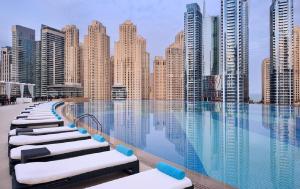 a pool with chaise lounges in front of a city skyline at Address Dubai Marina - 1B Apt, Full Marina View with 5 Star Hotel Facilities by Gardenia Suites in Dubai