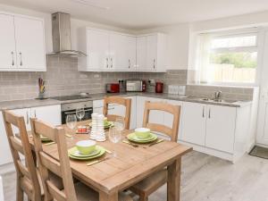 a kitchen with white cabinets and a wooden table with chairs at Clydfan Cottage in Llanerchymedd