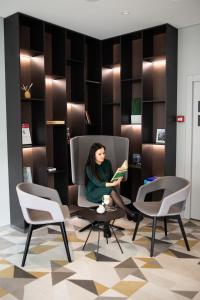 a woman sitting in a chair reading a book at Ibis Kaunas Centre in Kaunas