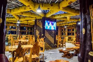 ein Restaurant mit Holztischen und -stühlen und einem TV an der Wand in der Unterkunft Lake Elementaita Nature Pebbles & Spar in Gilgil