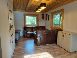 a living room with a leather couch and two windows at Słoneczny domek ze stawem i wędkowaniem in Żdżary