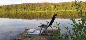 a chair sitting on a dock on a lake at Domki pod Dębami in Trzcianka