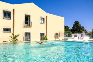 a person laying in a swimming pool next to a building at Hotel Baglio Di Scopello in Scopello