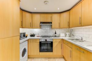 cocina con armarios de madera, lavadora y secadora en Redhill town centre apartment by Livingo, en Redhill