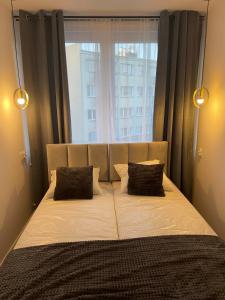 a bed with two pillows in front of a window at Apartament 80’s in Kołobrzeg