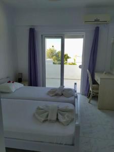 a white bedroom with two beds and a balcony at Plakia Beach Apartments in Pefki