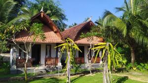 une maison avec un toit de chaume et des palmiers dans l'établissement Santhi Guna Bungalow, à Nusa Penida