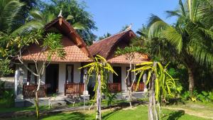 a house with a thatched roof and palm trees at Santhi Guna Bungalow in Nusa Penida