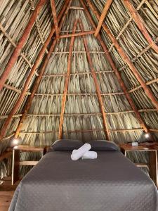 a bed in a thatched tent with two towels on it at Macarena Paredon in El Paredón Buena Vista