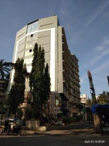 wysoki biały budynek z drzewami przed nim w obiekcie Kings International Juhu w Bombaju