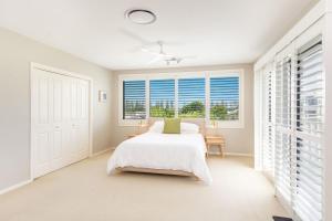 a white bedroom with a bed and two windows at Cowrie House - Spacious, Modern holiday home in Yamba