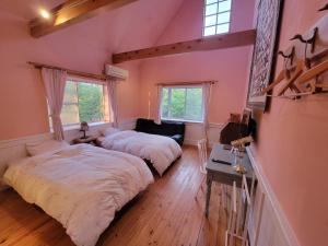 two beds in a bedroom with pink walls and wooden floors at Pension & Cafe Cruise in Shika