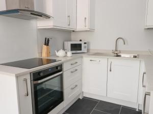 a kitchen with white cabinets and a black oven at Tyddyn Haidd in Amlwch