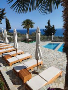 a row of lounge chairs with umbrellas next to a swimming pool at Perivolos Apartments in Dhërmi