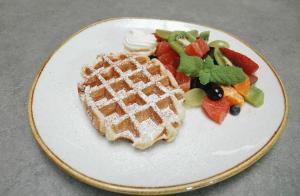 a white plate with a waffle and fruit on it at Hotel Patio Old Town in Wrocław