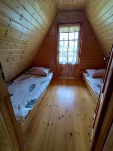 two beds in a wooden room with a window at Domki Noclegowe 693-664-683 in Solina