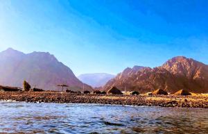 a group of huts on a beach with mountains in the background at SakraTah Camp - eco friendly in Taba