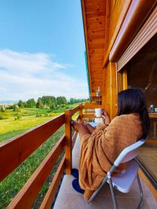 a woman sitting in a chair on a porch looking out at a field at Holiday Homes B&V in Žabljak