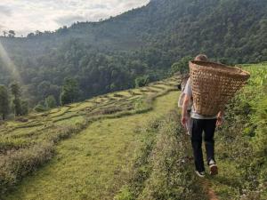 a man walking down a dirt road with a basket on his back at Village Homestay with Culture and Nature in Pokhara