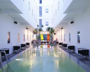 una piscina cubierta en un edificio con mesas y sillas en Amaris Hotel Sunset Road - Bali, en Kuta