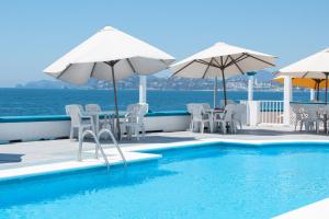 曼薩尼約的住宿－Hotel Caracoles，水边带椅子和遮阳伞的游泳池