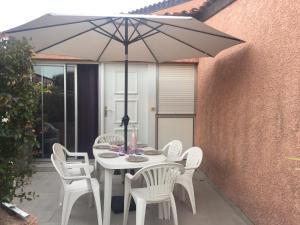 una mesa blanca con sillas blancas y una sombrilla en Maison dans résidence 3*proche plage, en Saint-Cyprien