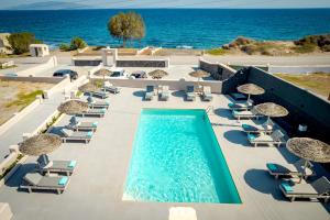 a pool with chairs and umbrellas next to the ocean at En Plo Boutique Suites in Oia