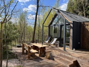 una terrazza in legno con tavolo, sedie e una casa in vetro di Odpoczynek Domki Pod Dębem z Opcją Jacuzzi a Ćmińsk