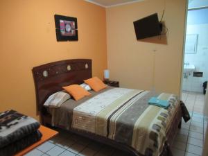 ein Schlafzimmer mit einem Bett mit orangefarbenen Kissen und einem TV in der Unterkunft Kurmi Hostel Lima Airport in Lima