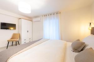 a white bedroom with a bed and a chair at Apartment Olive in Kaštela
