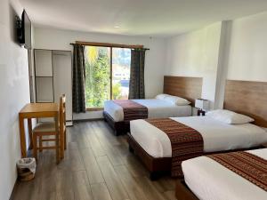 a hotel room with two beds and a desk and a window at Hotel El Geranio in Otavalo