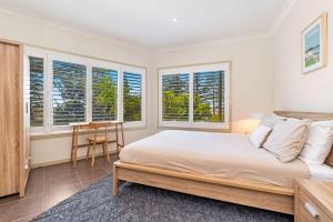 a bedroom with a bed and a table and windows at Seaspray 1 in Yamba